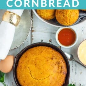 a cast iron skillet with cornbread on a white board with bowls of honey, butter, and cornbread muffins