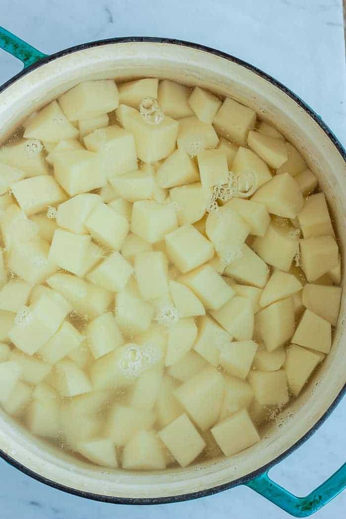 A teal saucepan with diced potatoes in water