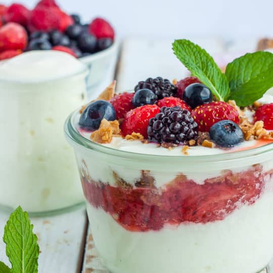 Two glass jars of yogurt topped with berries, granola, and mint