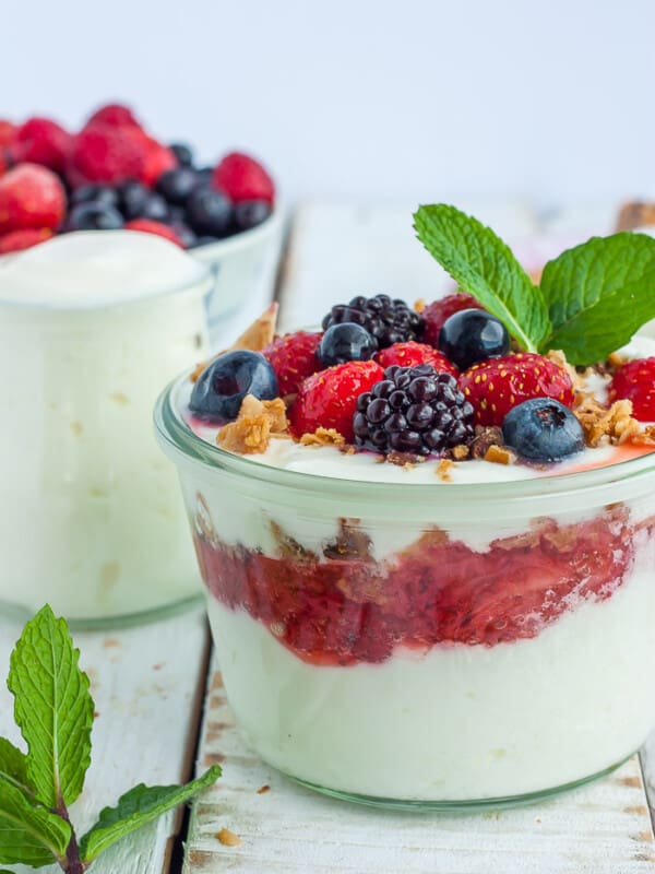 Two glass jars of yogurt topped with berries, granola, and mint