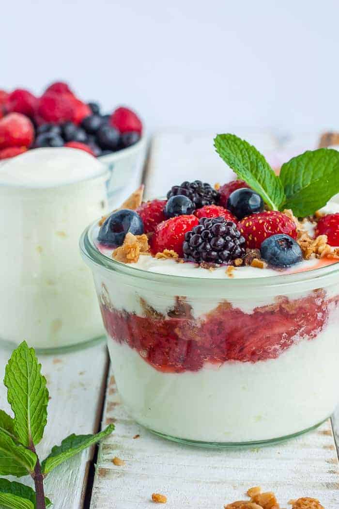 Two glass jars of yogurt topped with berries, granola, and mint