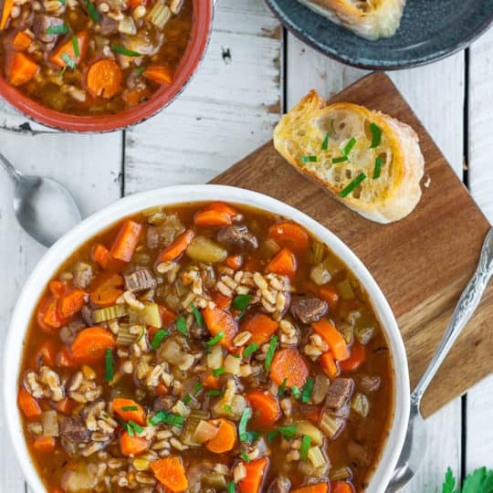 two bowls of beef barley soup with garlic bread.