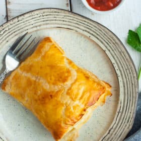 puff pastry pizza pockets sitting on plates with forks and dish of red sauce