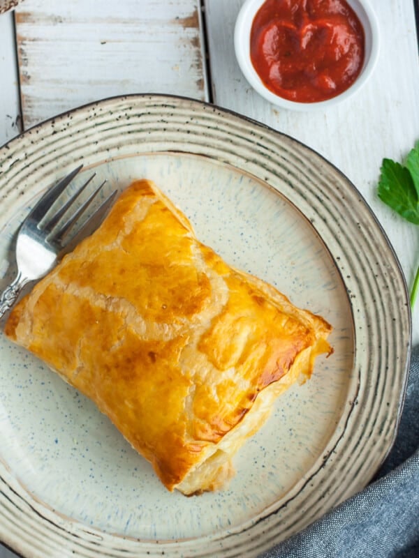 puff pastry pizza pockets sitting on plates with forks and dish of red sauce