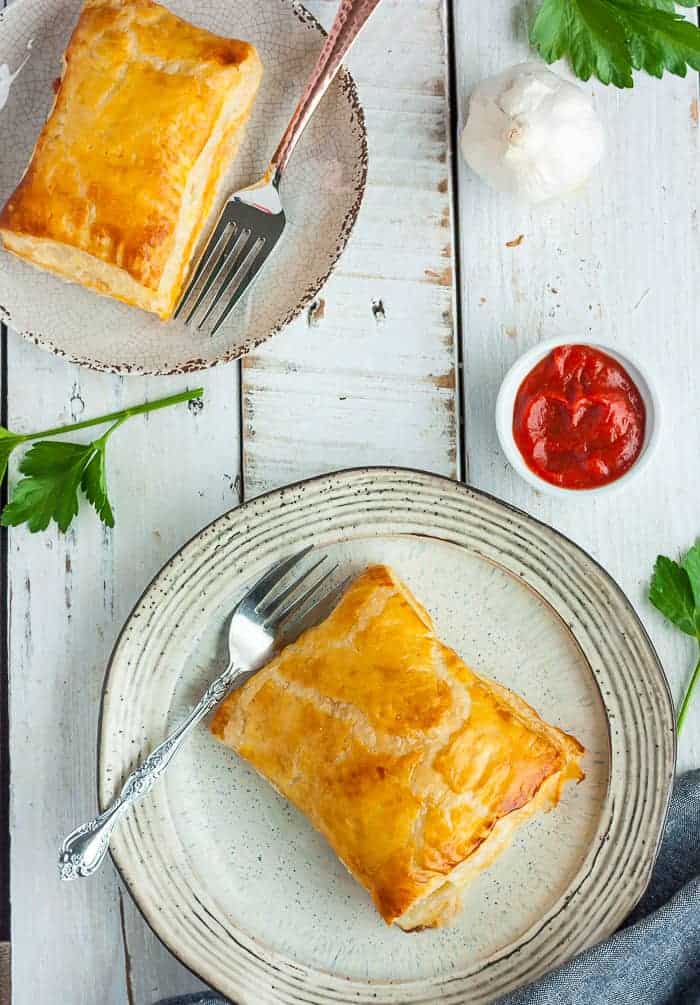 2 puff pastry pizza pockets sitting on plates with forks and dish of red sauce