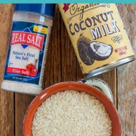 A bowl of rice, a shaker of salt, and a can of coconut milk on a wooden board
