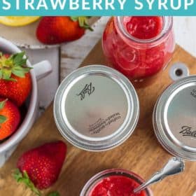 canning jars of strawberry syrup with lemons, fresh berries, and mint
