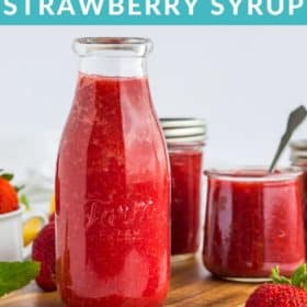 Mulitple glass jars of strawberry syrup on a wooden board with fresh strawberries and mint