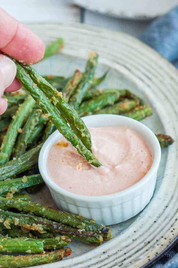 green bean fries being dipped into a small dish of dressing