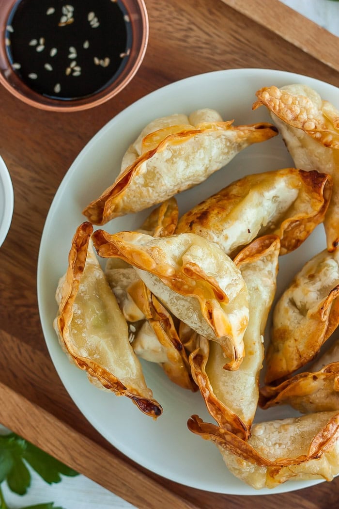 toasted air fryer potstickers on a white plate with a small bowl of dipping sauce.