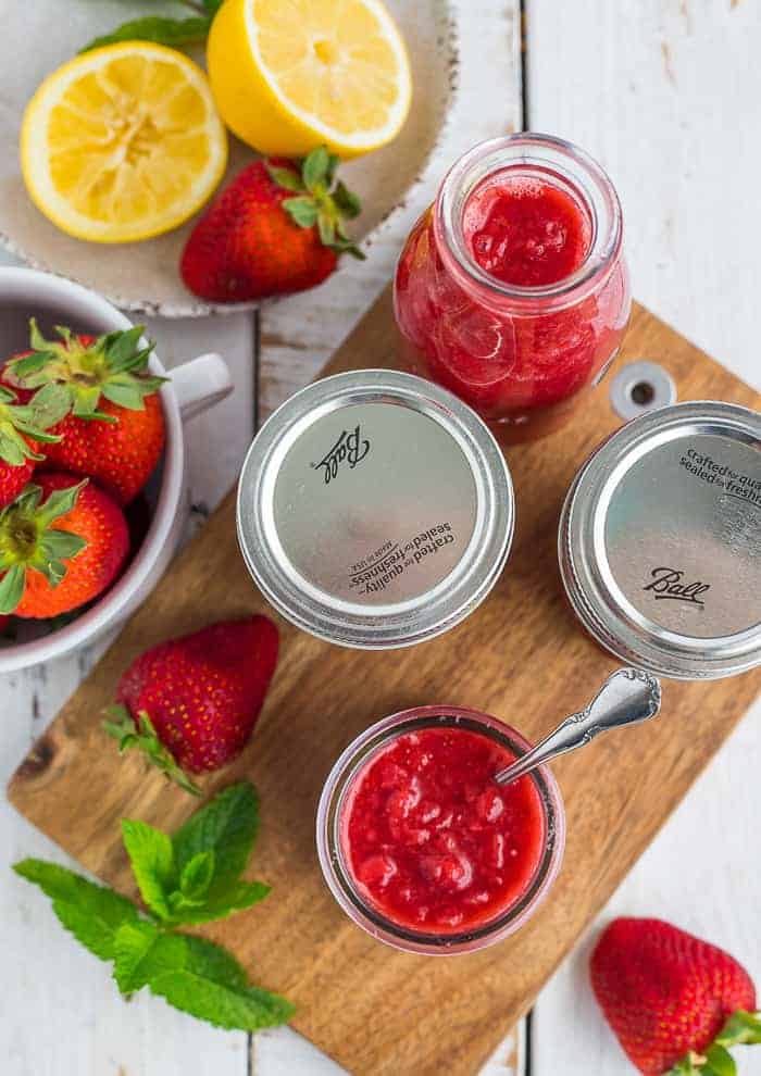canning jars of strawberry syrup with lemons, fresh berries, and mint