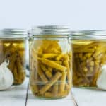 jars of green beans with a head of garlic on a white board