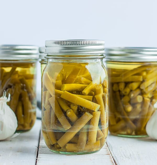 jars of green beans with a head of garlic on a white board