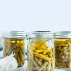 jars of green beans with a head of garlic on a white board