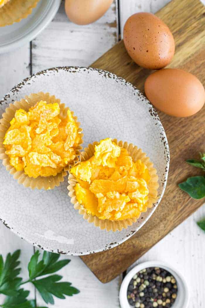 Frozen scrambled eggs on a grey plate on a cutting board with two whole eggs