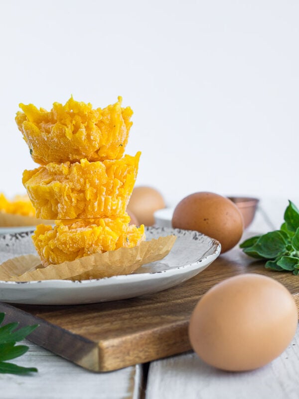 three stacks of frozen scrambled eggs on a plate, with fresh eggs and parsley on a white board.