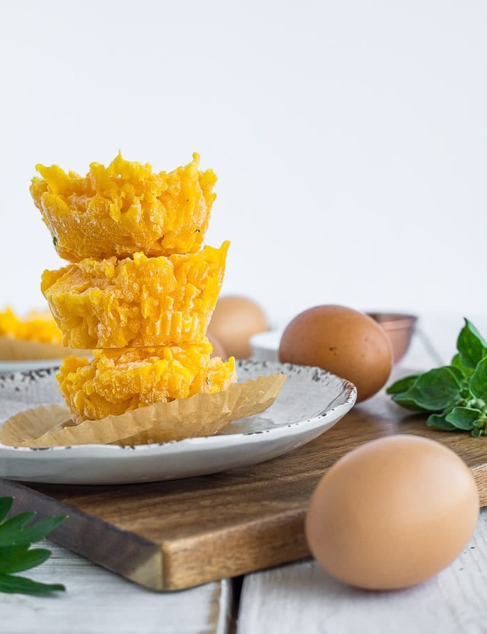 three stacks of frozen scrambled eggs on a plate, with fresh eggs and parsley on a white board.