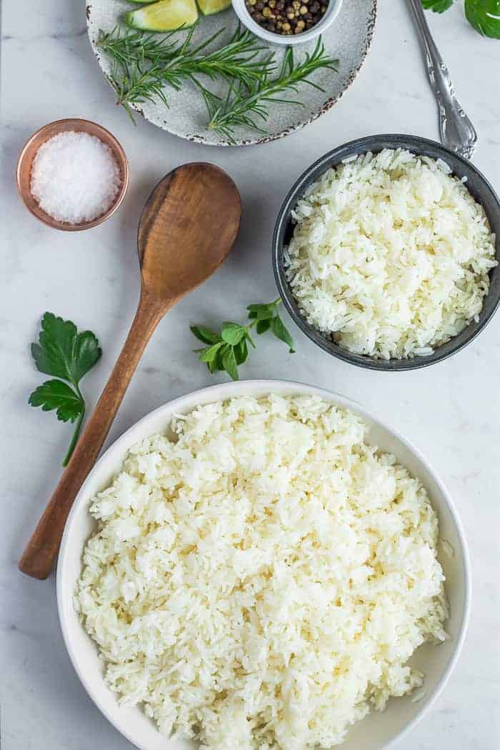 2 bowls of white rice on a white board with seasonings and a wooden spoon