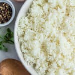 A white bowl with jasmine rice and small bowls of seasonings with a wooden spoon