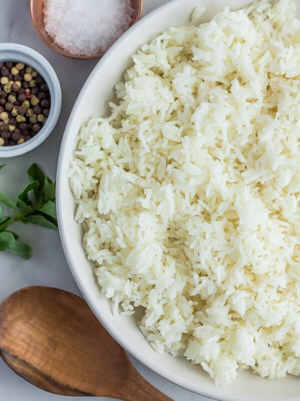 A white bowl with jasmine rice and small bowls of seasonings with a wooden spoon