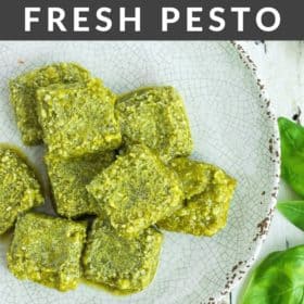 cubes of frozen pesto on a grey plate with fresh basil on a white board