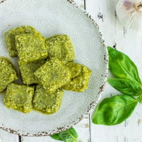 cubes of frozen pesto on a grey plate with fresh basil on a white board