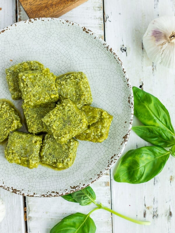 cubes of frozen pesto on a grey plate with fresh basil on a white board