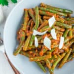 a grey bowl with green beans in tomato sauce topped with shaved parmesan