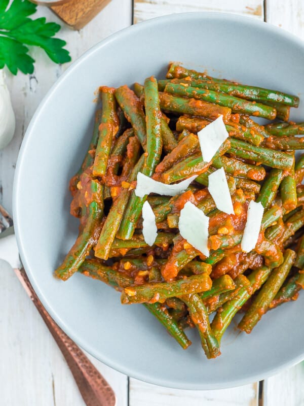 a grey bowl with green beans in tomato sauce topped with shaved parmesan