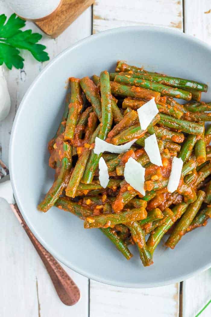 a grey bowl with green beans in tomato sauce topped with shaved parmesan