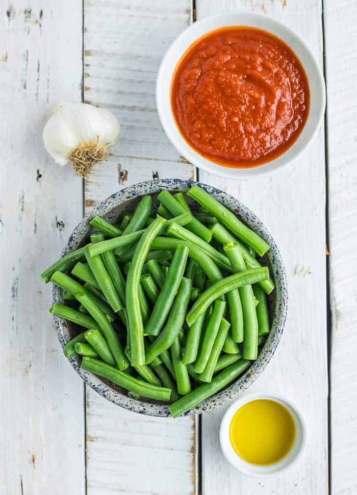 a bowl of green beans, tomato sauce, olive oil, and a head of garlic