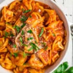 a white bowl of tortellini topped with chopped basil
