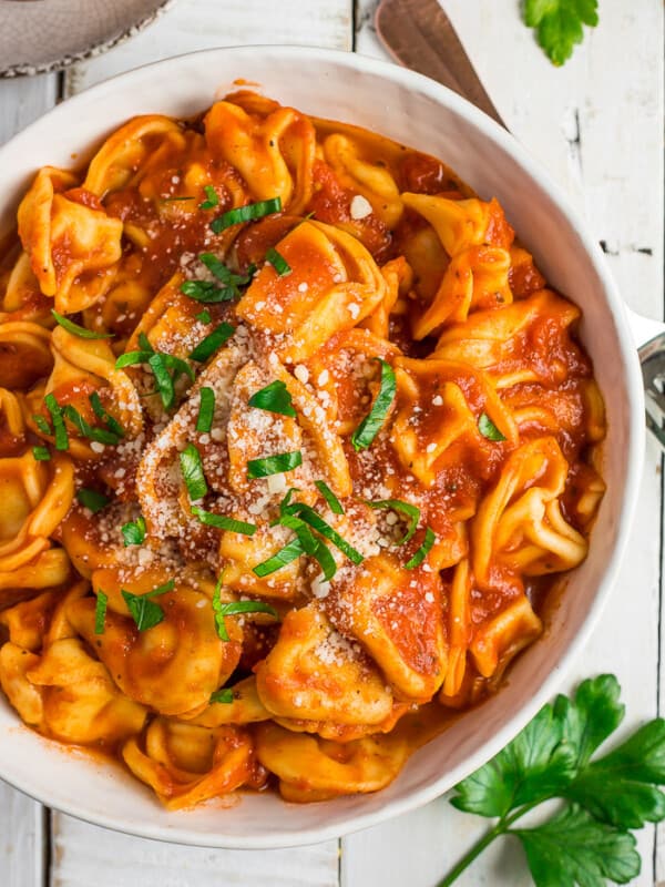 a white bowl of tortellini topped with chopped basil