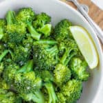 a bowl of green steamed broccoli with a lemon wedge