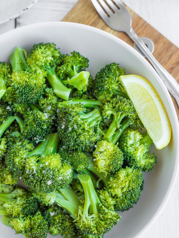 a bowl of green steamed broccoli with a lemon wedge