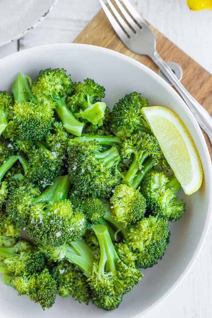 a bowl of green steamed broccoli with a lemon wedge