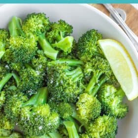 a bowl of green steamed broccoli with a lemon wedge