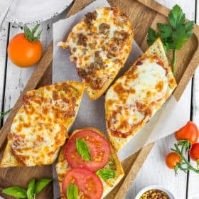 french bread pizzas on a wooden tray with tomatoes and other toppings on a white board