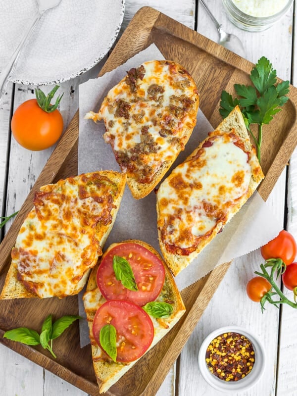 french bread pizzas on a wooden tray with tomatoes and other toppings on a white board