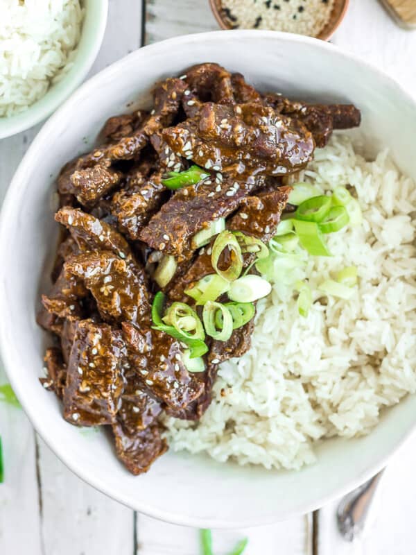 A white bowl of rice and Instant Pot teriyaki beef topped with green onions