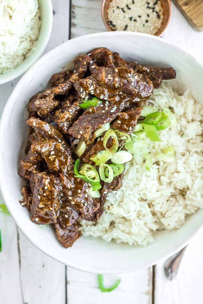 A white bowl of rice and Instant Pot teriyaki beef topped with green onions