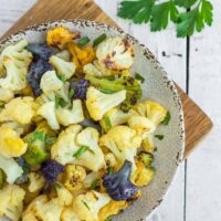 a plate with colorful roasted cauliflower on a white wooden board