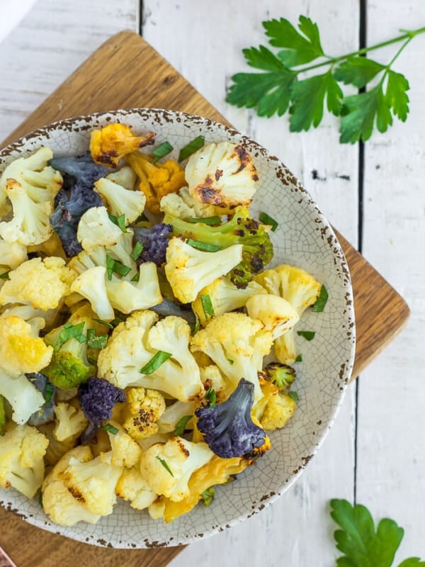 a plate with colorful roasted cauliflower on a white wooden board