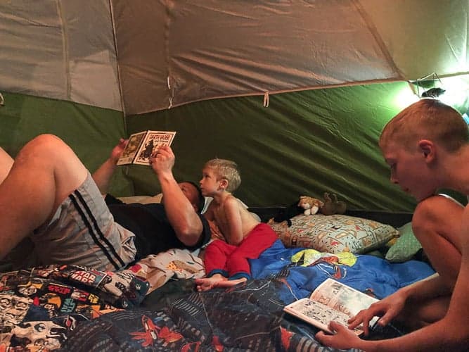 2 boys and a man reading in a tent