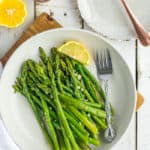a plate of asparagus with a fork and a lemon wedge