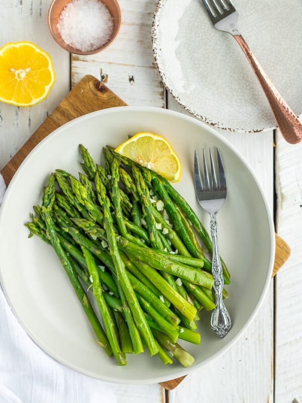 a plate of asparagus with a fork and a lemon wedge