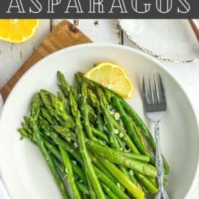 a plate of asparagus with a fork and a lemon wedge