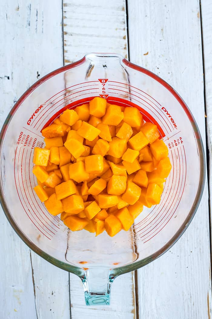 cubes of winter squash in a glass mixing bowl on a wooden surface.