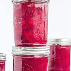 3 jars of homemade canned cranberry sauce with fresh cranberries on a white board