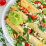 a plate of air fryer taquitos topped with cilantro, tomatoes, and guacamole